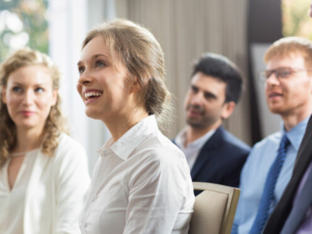 Young businesswoman and her male and female colleagues smiling, sitting and watching presentation in conference room